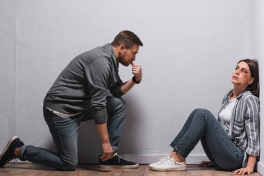 Yüzünde morluklar olan korkmuş bir kadın yerde yatan düşünceli, tacizci kocaya bakıyor. 