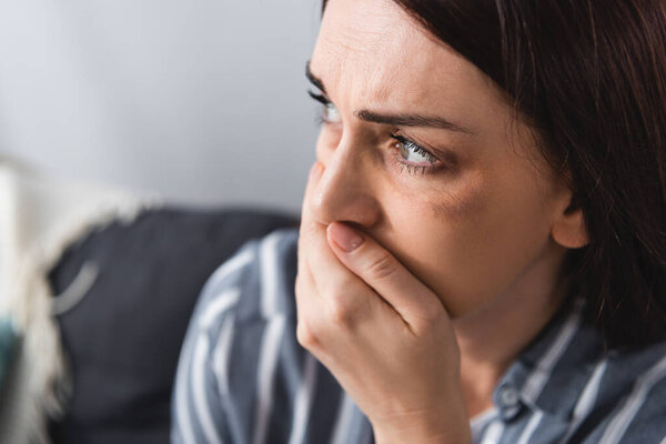 Испуганная женщина с синяком на лице, покрывающим рот рукой дома 