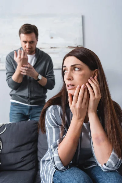 Scared Victim Domestic Violence Bruise Cheek Sitting Couch Husband Blurred — Stock Photo, Image