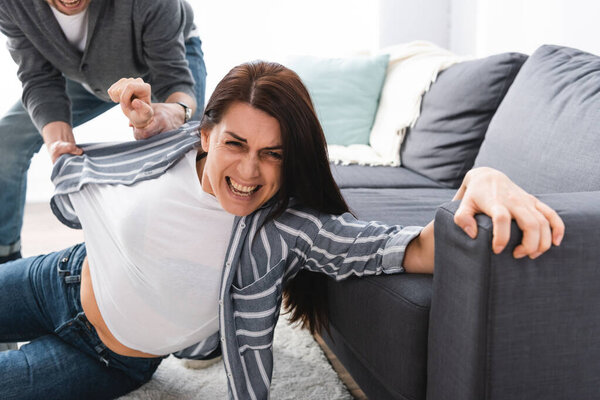 Frightened woman lying on floor near abusive husband holding hand on blurred background 