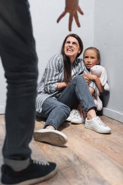 Screaming woman with bruises and kid with soft toy looking at abusive father on blurred foreground  clipart
