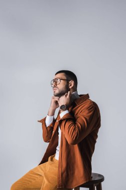 Gözlüklü şık adam, gri sandalyedeki balıkçı yaka kazağı ayarlıyor. 