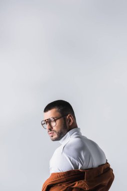 Beyaz balıkçı yakalı ve ceketli şık bir adam. Gri üzerine tek başına bakıyor. 