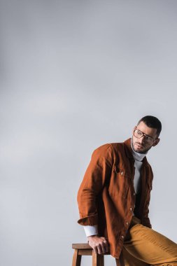 Genç şık adam, gri sandalyenin yanından uzaklara bakıyor. 