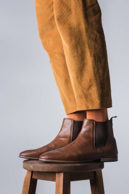 Gri sandalyede izole edilmiş kahverengi ayakkabılı şık adamın bacakları. 