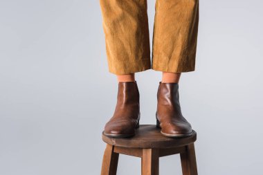 Kahverengi ayakkabılı, tahta sandalyeli, gri renkli bir adamın bacakları. 