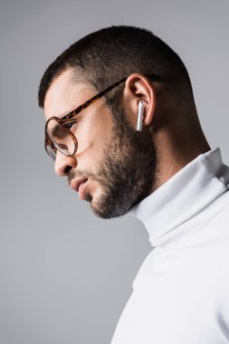 Gözlüklü şık bir adam ve beyaz balıkçı yakalı. Gri kulaklıklı kablosuz kulaklıkla müzik dinliyor. 