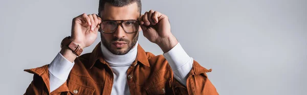 Serious Stylish Man Adjusting Eyeglasses Looking Camera Isolated Grey Banner — Stock Photo, Image