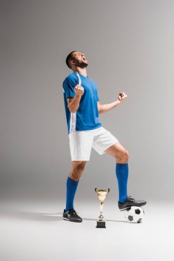 Sporcu, gri arka planda futbol ve şampiyonlar kupasının zaferini kutluyor 