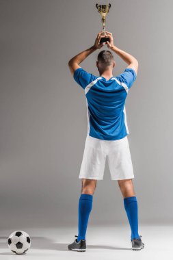 Gri arkaplanda futbolda altın kupa tutan sporcunun arka plan görüntüsü 