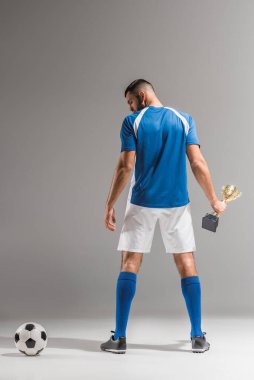 Şampiyonlar kupasıyla arka plandaki sporcu gri arka planda futbola bakıyor. 