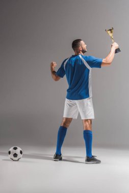 Gri arka planda futbolda altın kupa tutan gülümseyen sporcunun arka plan görüntüsü 
