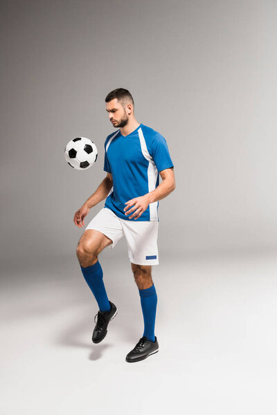 Bearded sportsman playing soccer on grey background