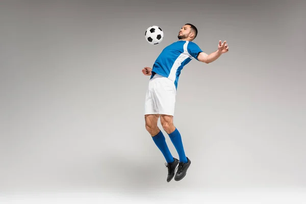 Sportman Training Met Voetbal Tijdens Het Springen Grijze Achtergrond — Stockfoto