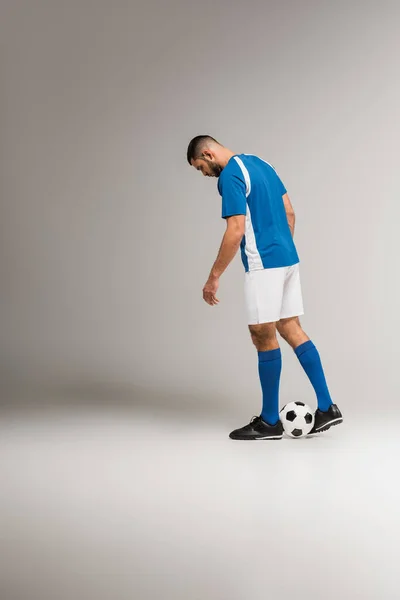 Γενειοφόρος Αθλητής Κοιτάζοντας Ποδόσφαιρο Ενώ Στέκεται Γκρι Φόντο — Φωτογραφία Αρχείου