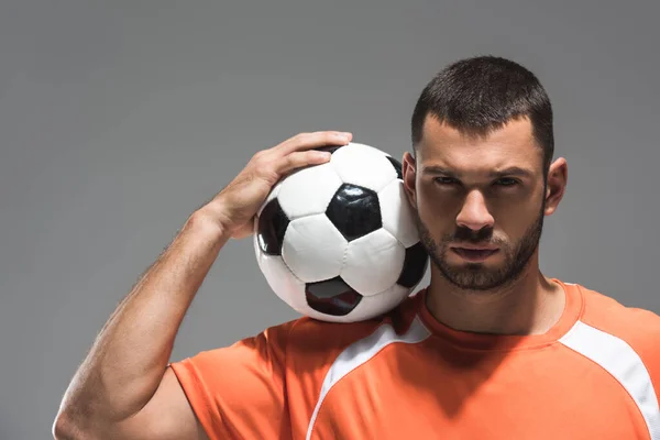 頭の近くにサッカーを保持し 灰色で隔離されたカメラを見てひげそりのスポーツマン — ストック写真