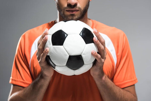 Обрезанный вид футбола в руках бородатого спортсмена на размытом фоне изолирован на сером