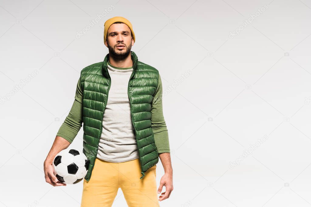 Bearded sportsman holding football and looking at camera isolated on grey 