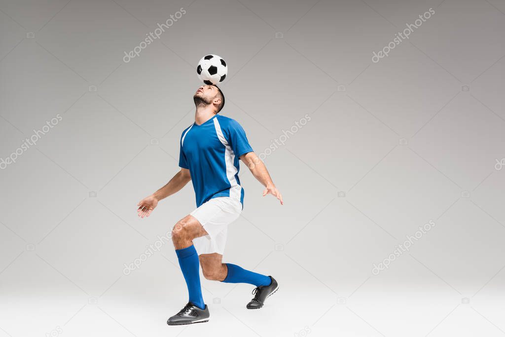 Sportsman holding football on head while balancing on grey background 