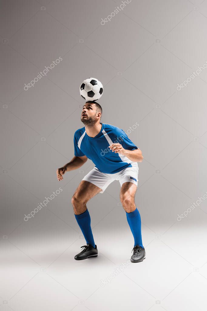 Bearded sportsman balancing with football on head on grey background 