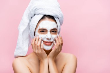 beautiful woman with towel on head and clay mask on face isolated on pink clipart