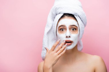 Şok olmuş güzel bir kadın, kafasında havlu, yüzünde kilden bir maske, pembe renkte izole edilmiş.