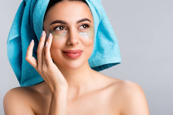 smiling beautiful woman with blue towel on hair and hydrogel eye patches on face isolated on grey