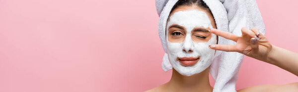 beautiful woman with towel on head and clay mask on face grimacing isolated on pink, banner