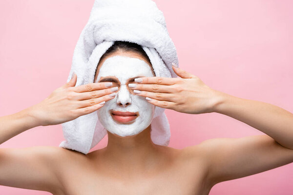 beautiful woman with towel on head and clay mask on face covering eyes isolated on pink