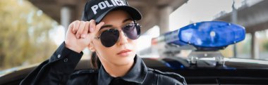 Kendine güvenen genç bir polis memurunun portresi. Arka planda bulanık bir şekilde devriye arabasının yanından uzağa bakıyor.