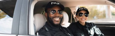 Mutlu çok kültürlü polis memurları bulanık arka planda devriye arabasındaki kameraya bakıyor.