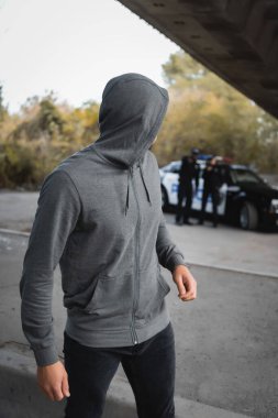 Kapüşonlu hırsız arka planda bulanık, çok kültürlü polis memurlarıyla dışarı bakıyor.