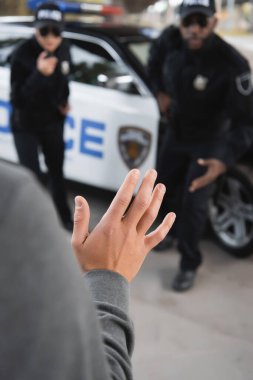 close up view of offender showing hand with blurred multicultural police officers on background outdoors clipart
