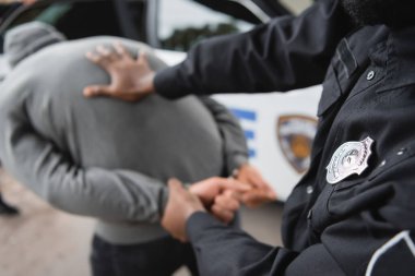 Afro-Amerikan polisi, bulanık arka planda kapüşonlu suçluyu tutukladı.