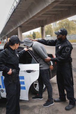 Afro-Amerikan polisi, kapüşonlu suçluyu iş arkadaşı ve devriye arabasının yakınında tutukladı.