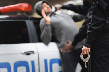 Arka planda çok kültürlü polis ve suçluyla elleri kelepçeli bir polis memuru var.