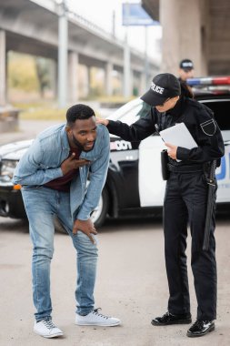 Afro-Amerikan kurbanını sakinleştiren, arka planı bulanık, nefes darlığı çeken bir kadın polis.