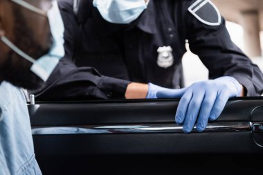 Plastik eldivenli bir polisin tıbbi maske takmış Afro-Amerikan bir sürücünün yanında dikilirken görüntüsü bulanık. 