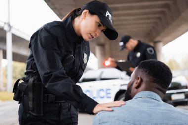 Siyahi Amerikalıyı sakinleştiren bir kadın polis. Şehir sokağının bulanık arka planında iş arkadaşının yanında. 