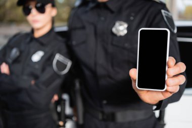 Bulanık arkaplan üzerinde polis memurunun yanındaki boş ekranlı akıllı telefon.