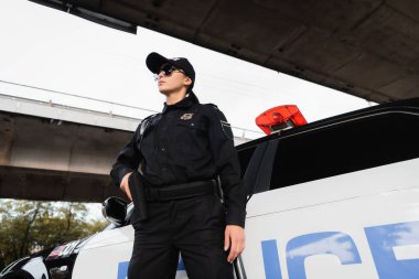 Güneş gözlüklü kadın, şehir sokağındaki arabanın yanında silah kılıfında. 
