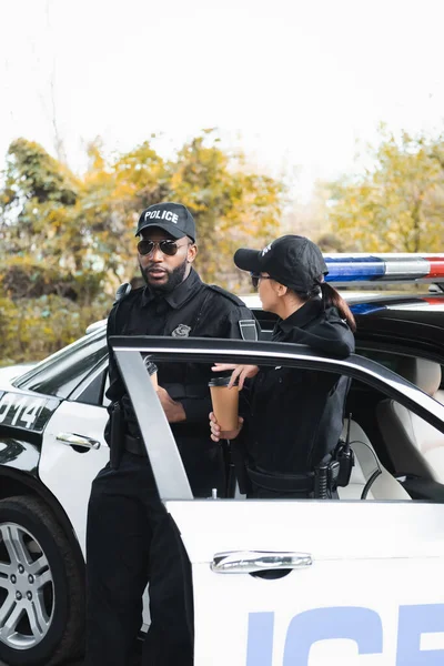 Multiculturele Politieagenten Met Papieren Kopjes Praten Terwijl Leunend Patrouille Auto — Stockfoto