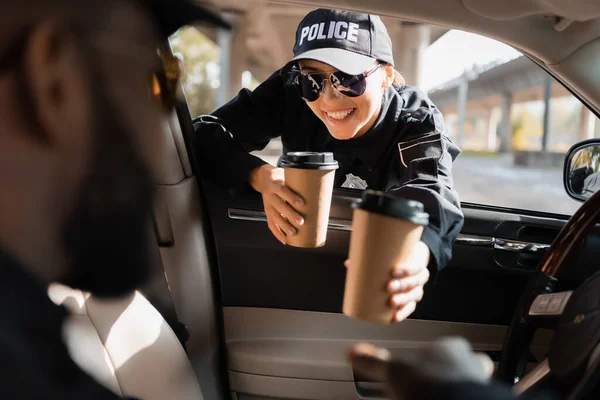Щаслива Поліцейська Дає Паперову Чашку Афроамериканському Колезі Патрульній Машині Розмитому — стокове фото