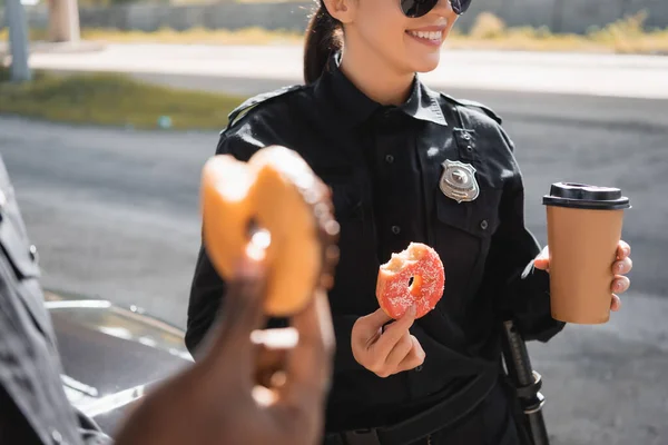 ドーナツと紙コップを持つ警察官のクロップドビュー屋外でぼやけた前景に — ストック写真