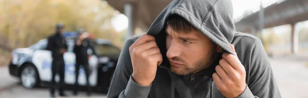 Scared Hooded Offender Hiding Blurred Police Officers Background Outdoors Banner — Stock Photo, Image