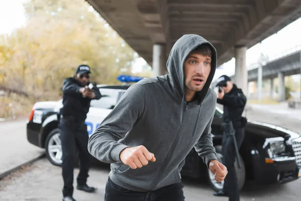 Rémült Kapucnis Bűnöző Menekül Multikulturális Rendőrtisztek Célzás Pisztollyal Homályos Háttér — Stock Fotó