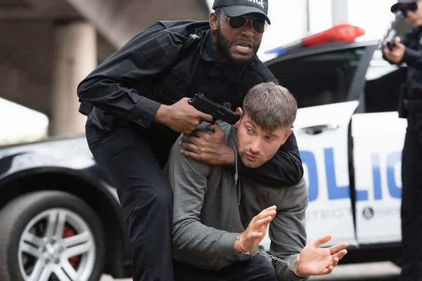 Policía Afroamericano Enojado Apuntando Con Pistola Delincuente Esposado Sobre Fondo —  Fotos de Stock