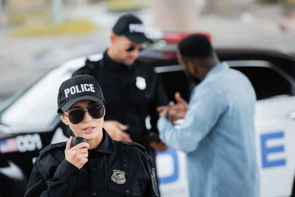 Junge Polizistin Spricht Radio Set Mit Verschwommenem Kollegen Und Afrikanisch — Stockfoto