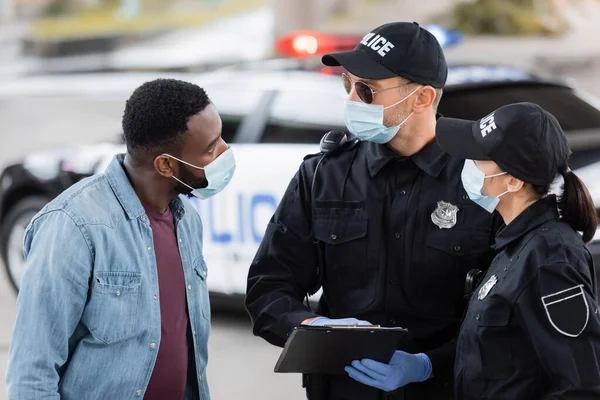 Policiais Máscaras Médicas Com Prancheta Olhando Para Vítima Afro Americana — Fotografia de Stock