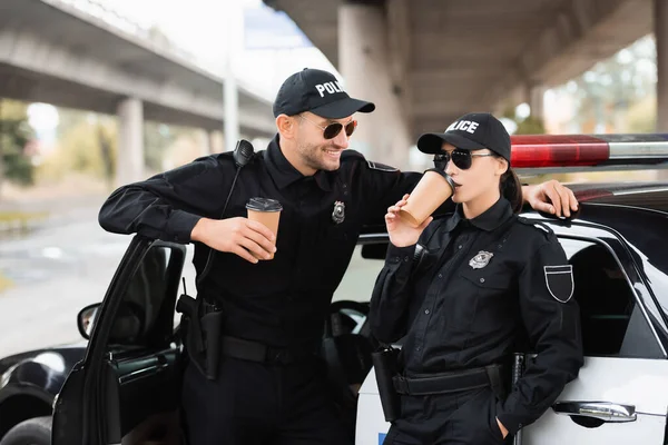 戴着太阳镜微笑的警官看着同事们喝咖啡 然后走近外面的汽车 — 图库照片